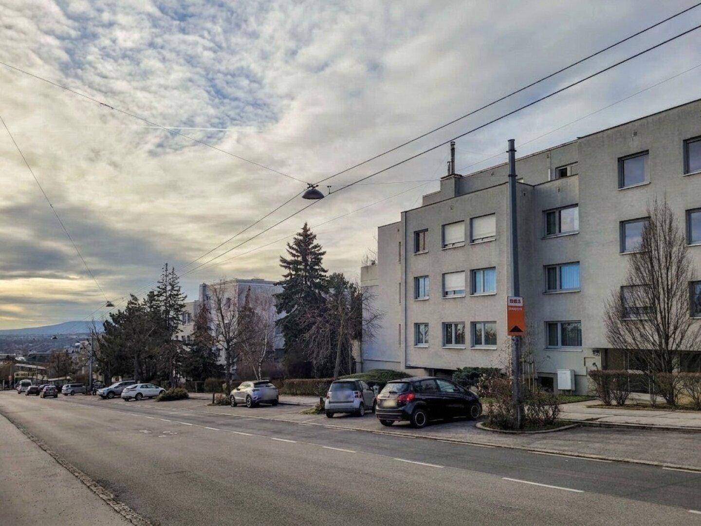 Straßenansicht eines Wohngebäudes mit parkenden Autos und einem weiten Blick in die Ferne.