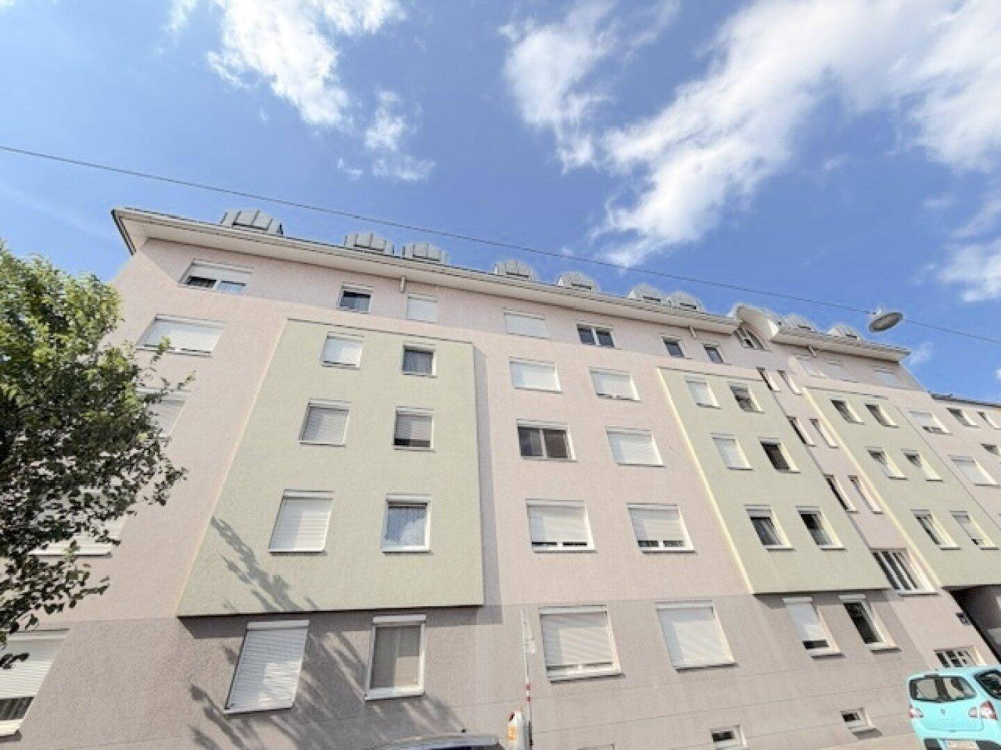 Mehrstöckiges Wohngebäude mit heller Fassade und zahlreichen Fenstern unter blauem Himmel.