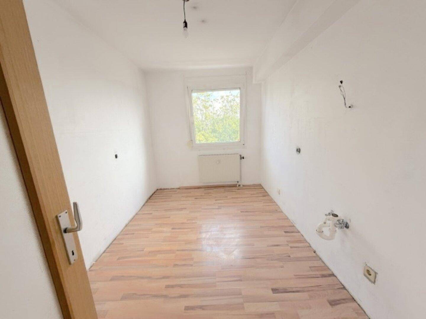Leerer Raum mit Laminatboden und Fenster, vorbereitet für individuelle Nutzung.