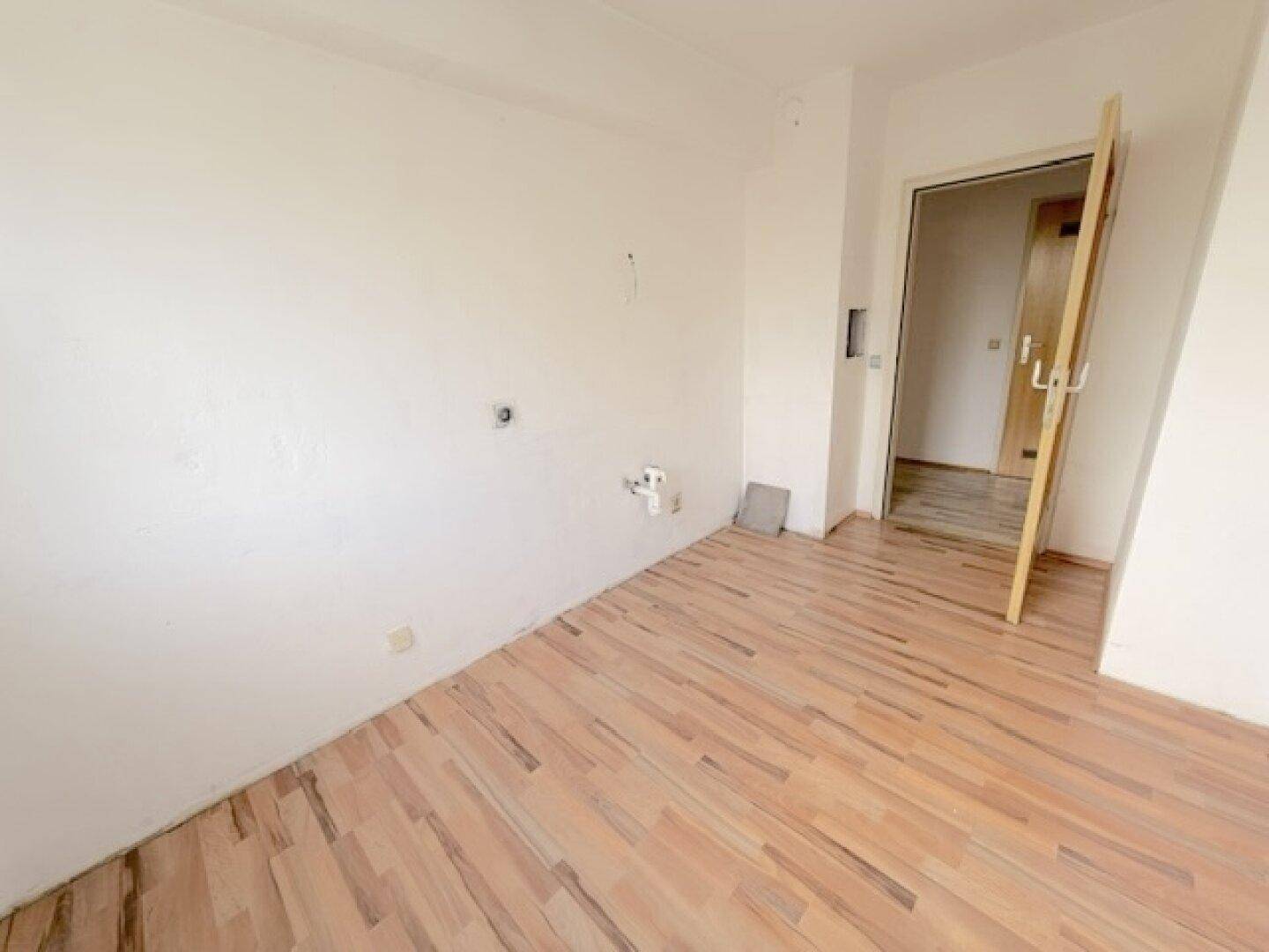 Heller, leerer Raum mit Laminatboden und Türöffnung, bereit zur individuellen Gestaltung.
