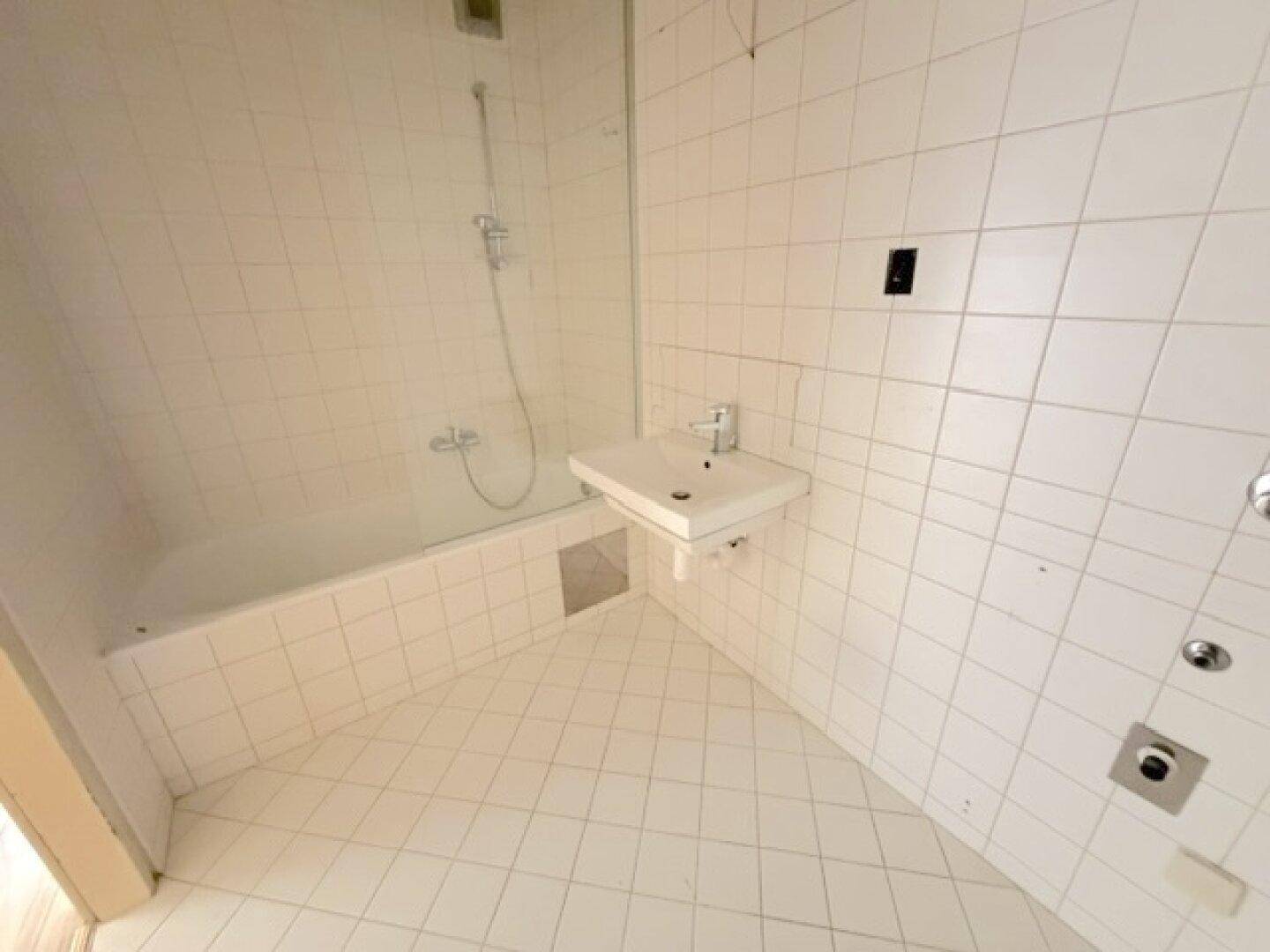 Helles Badezimmer mit weißen Fliesen, Badewanne und modernem Waschbecken.