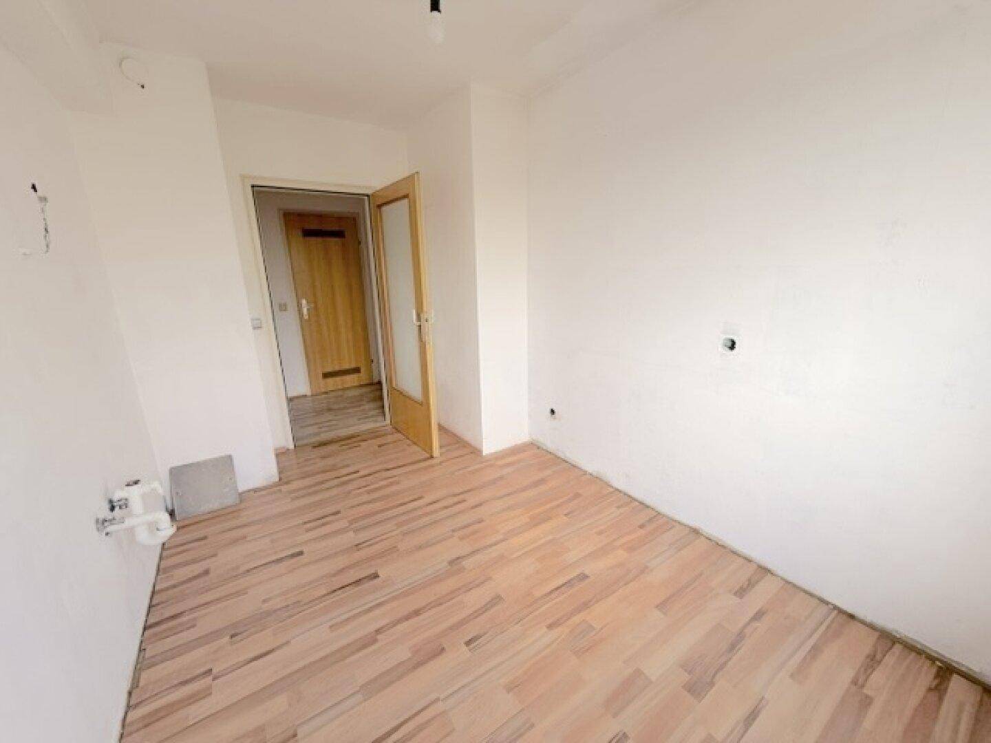 Leerer Raum mit Laminatboden und Tür, bietet flexible Nutzungsmöglichkeiten.