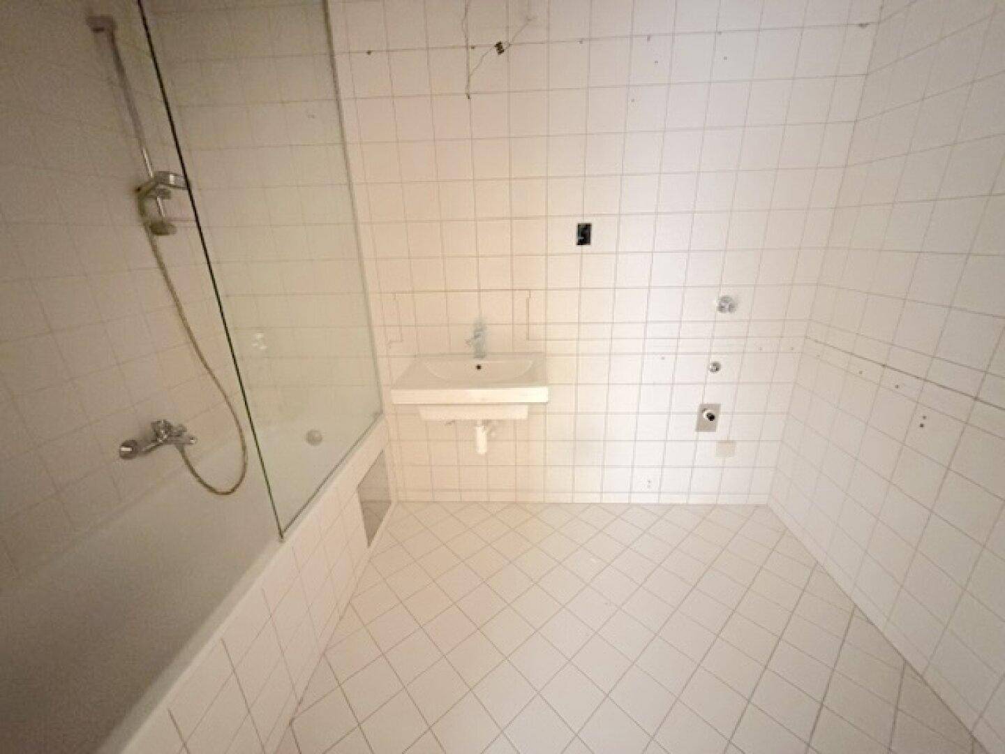 Badezimmer mit weißen Fliesen, Badewanne mit Duschwand und Waschbecken.