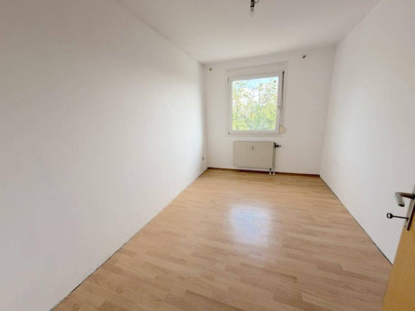 Leeres Schlafzimmer mit Laminatboden und Fenster, bietet viel Tageslicht.