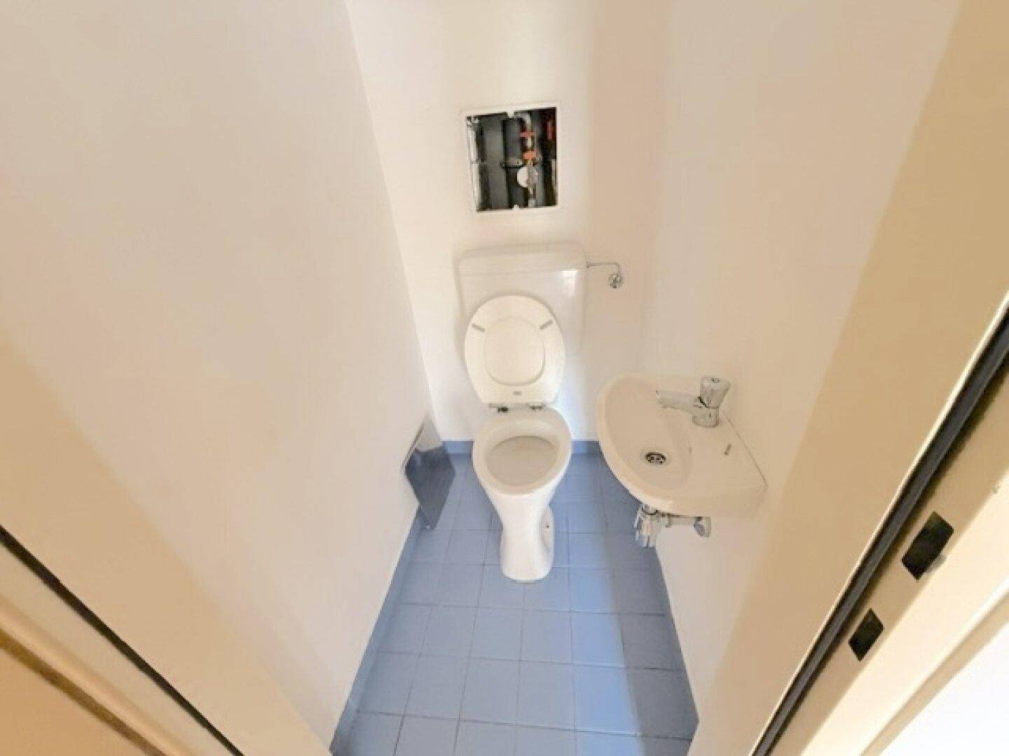 Kleines Gäste-WC mit Toilette, Waschbecken und blauen Bodenfliesen.
