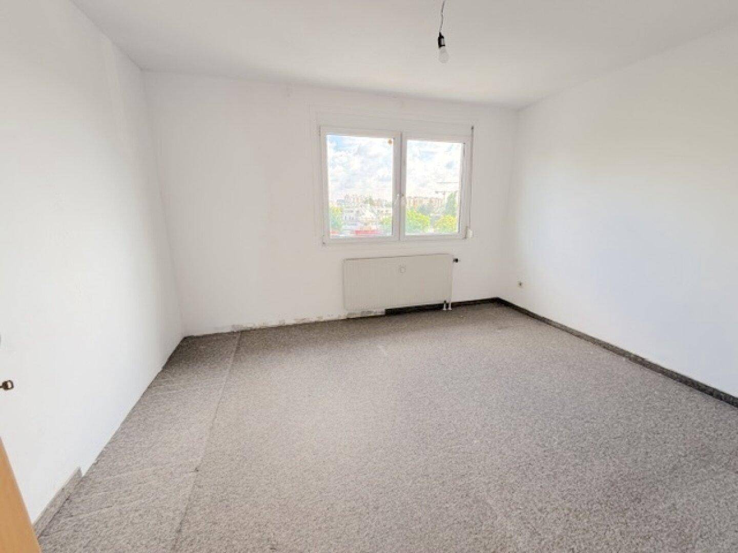 Leeres Schlafzimmer mit grauem Teppichboden und Fenster, bietet eine neutrale Basis.