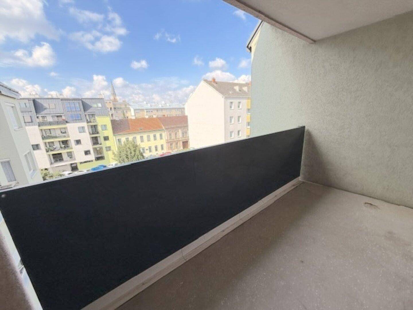 Unmöblierter Balkon mit Blick auf die städtische Umgebung und den blauen Himmel.