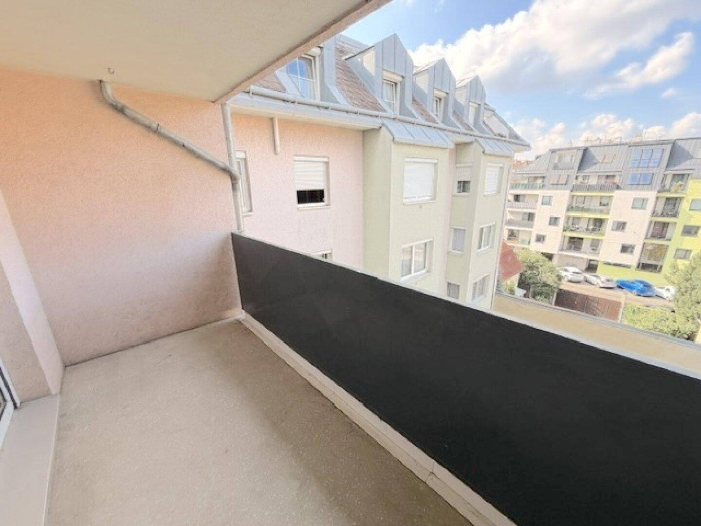 Balkon mit Ausblick auf die umliegenden Gebäude und den Himmel, unmöbliert.