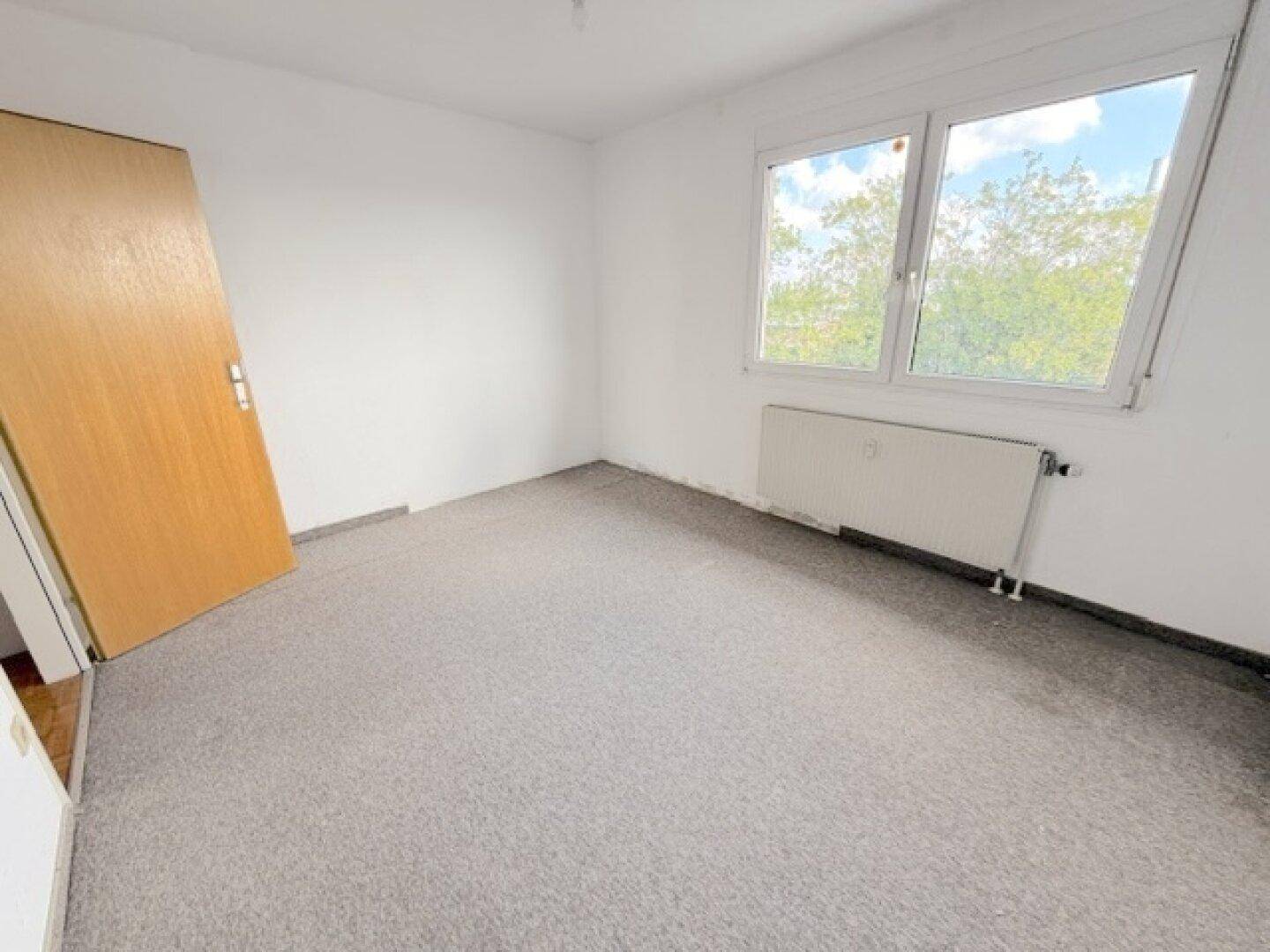 Leeres Schlafzimmer mit grauem Teppichboden und Fenster, bietet eine ruhige Atmosphäre.