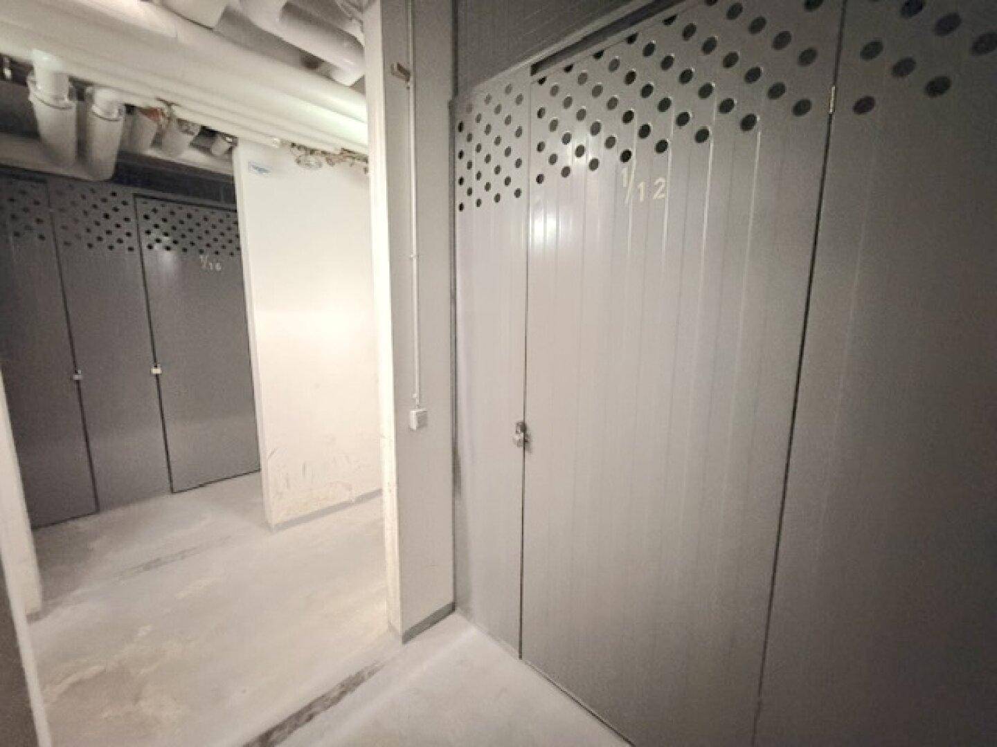 Kellerabteile mit Metalltüren in einem gut beleuchteten Untergeschoss für zusätzlichen Stauraum.