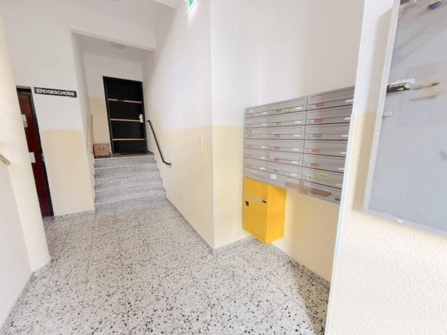 Eingangsbereich mit Briefkästen, Treppenaufgang und Fliesenboden im Erdgeschoss des Gebäudes.