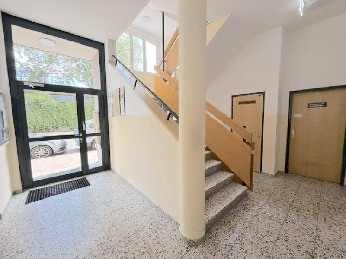 Heller Eingangsbereich mit Treppenaufgang, Fliesenboden und großer Glastür zum Außenbereich.
