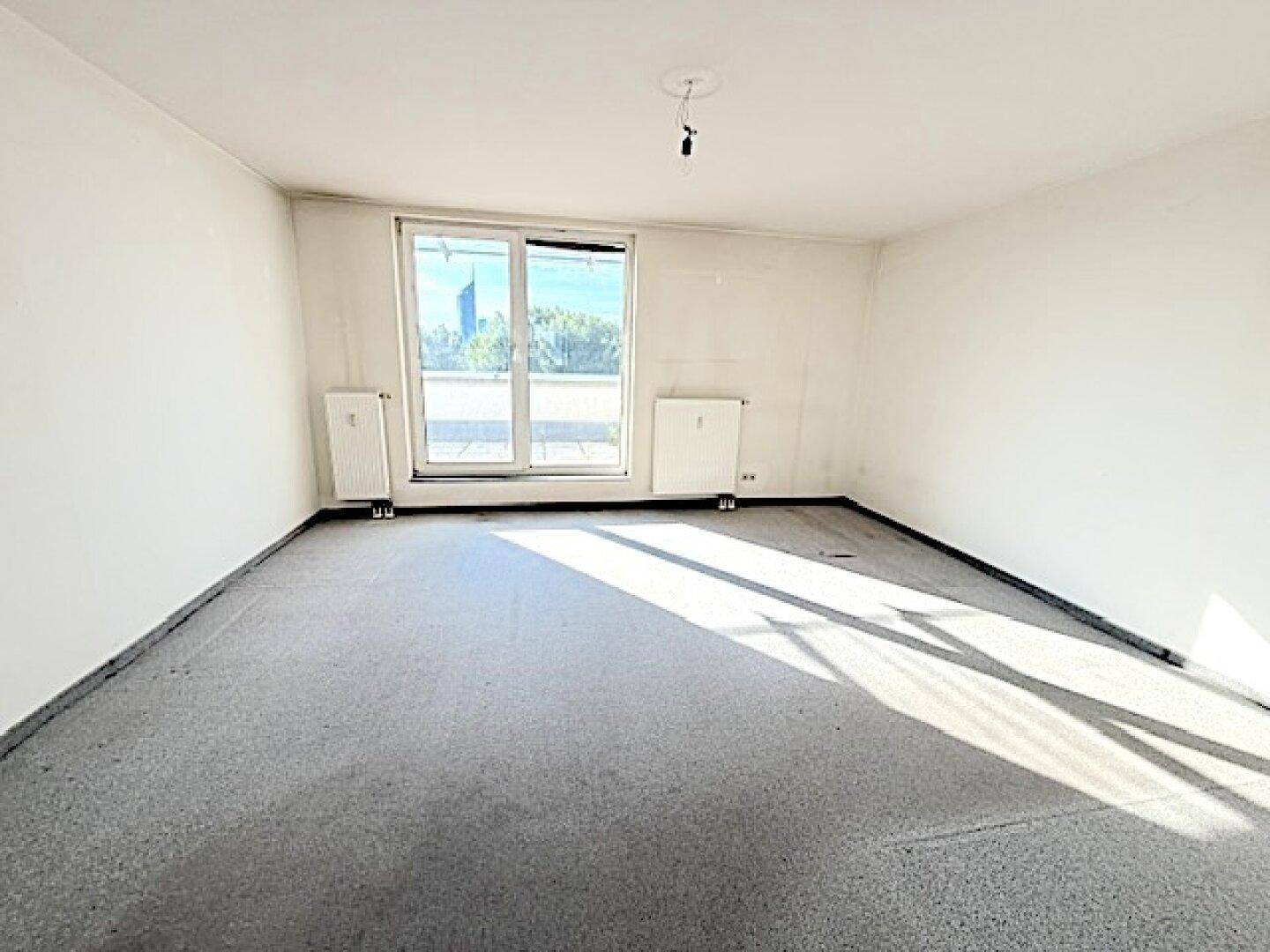 Heller Raum mit Teppichboden und großem Fenster, das viel Tageslicht hereinlässt.