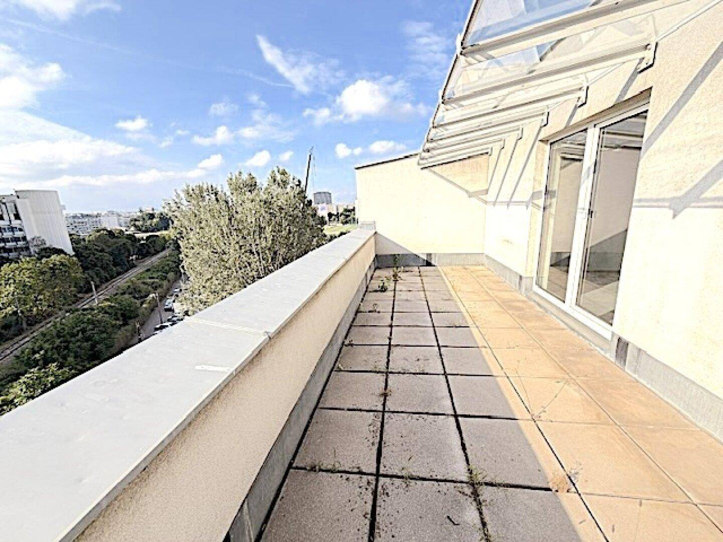 Geräumige Terrasse mit Fliesenboden und Blick auf die umliegende Stadtlandschaft und Bäume.