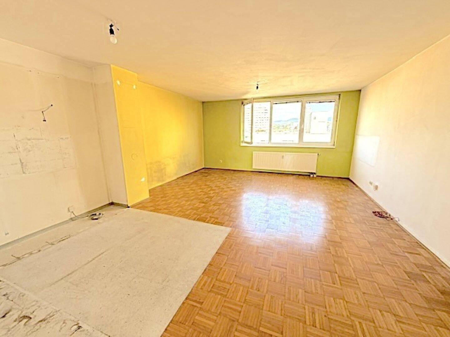 Geräumiges Zimmer mit Fischgrätparkett und farbigen Wänden, bereit für eine Renovierung.