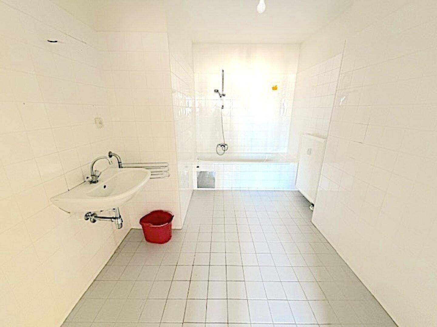 Gefliestes Badezimmer mit Badewanne, Duschvorrichtung und Waschbecken in schlichtem Design.