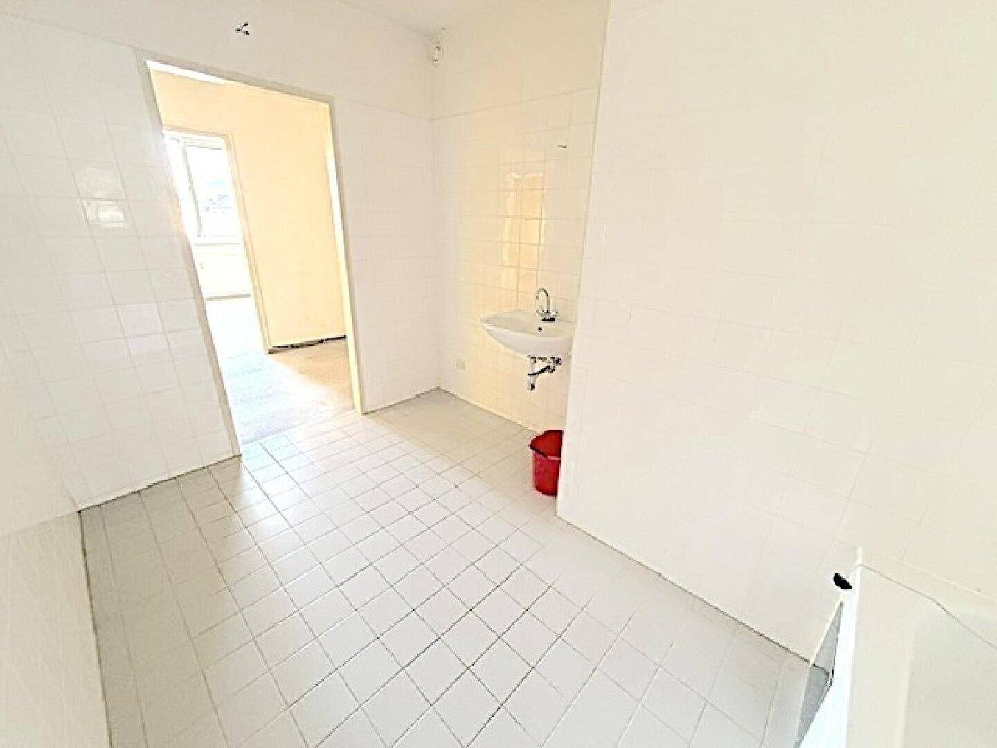Weiß gefliestes Badezimmer mit Waschbecken und Blick in den angrenzenden Raum.