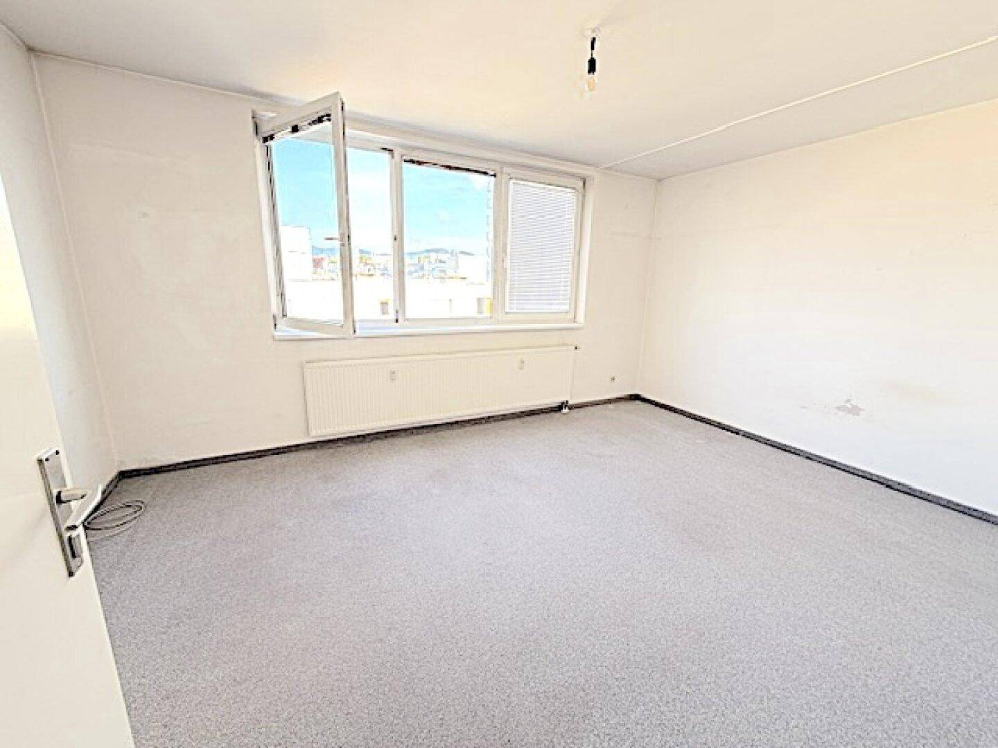 Helles Schlafzimmer mit Teppichboden und geöffnetem Fenster, das frische Luft hereinlässt.