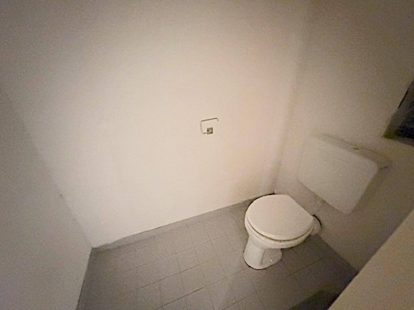 Kleines WC mit Fliesenboden und einfacher Toilette, ideal als Gästetoilette.