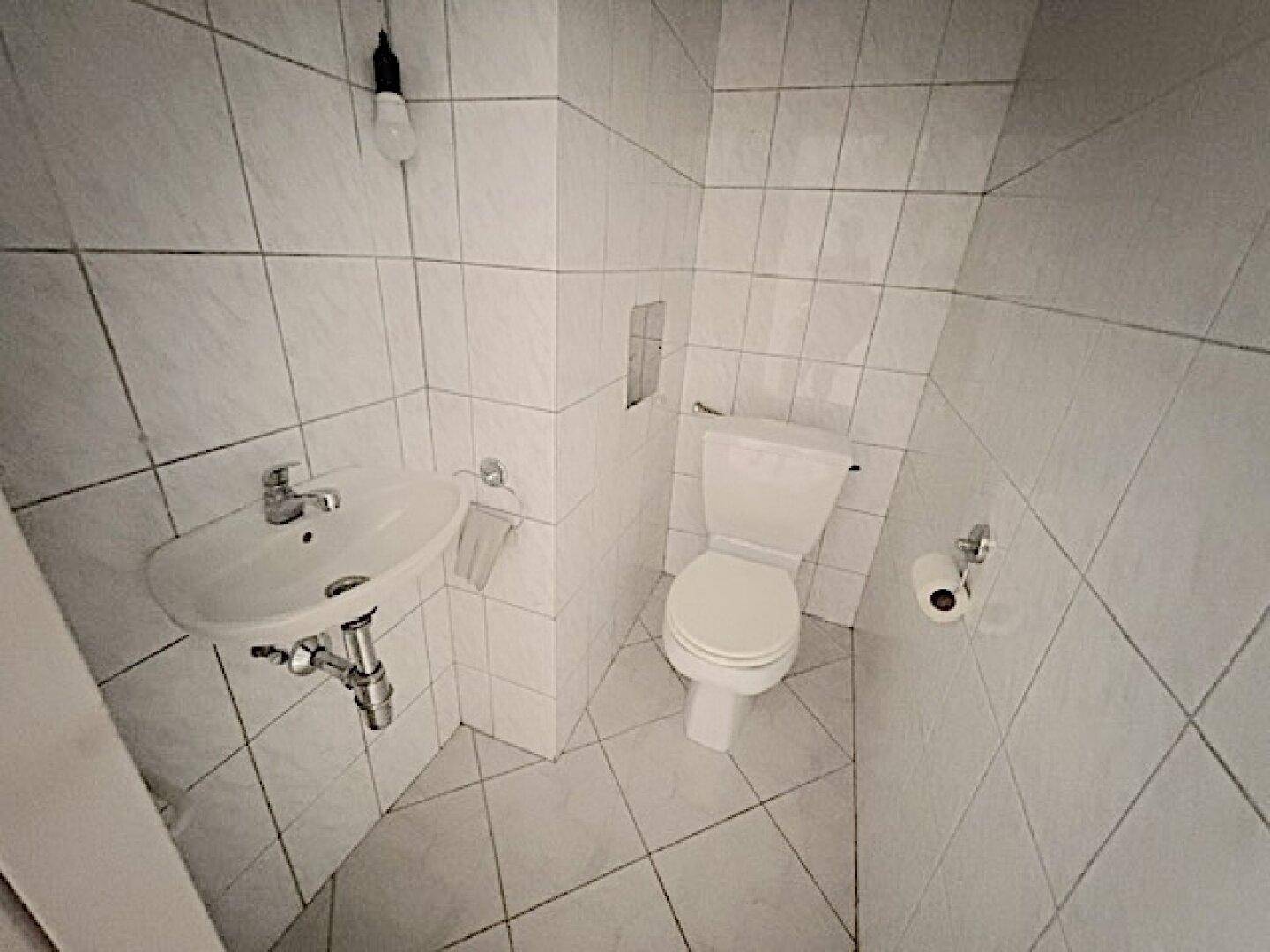 Kleines Gäste-WC mit weiß gefliesten Wänden und Boden, ausgestattet mit Waschbecken und Toilette.