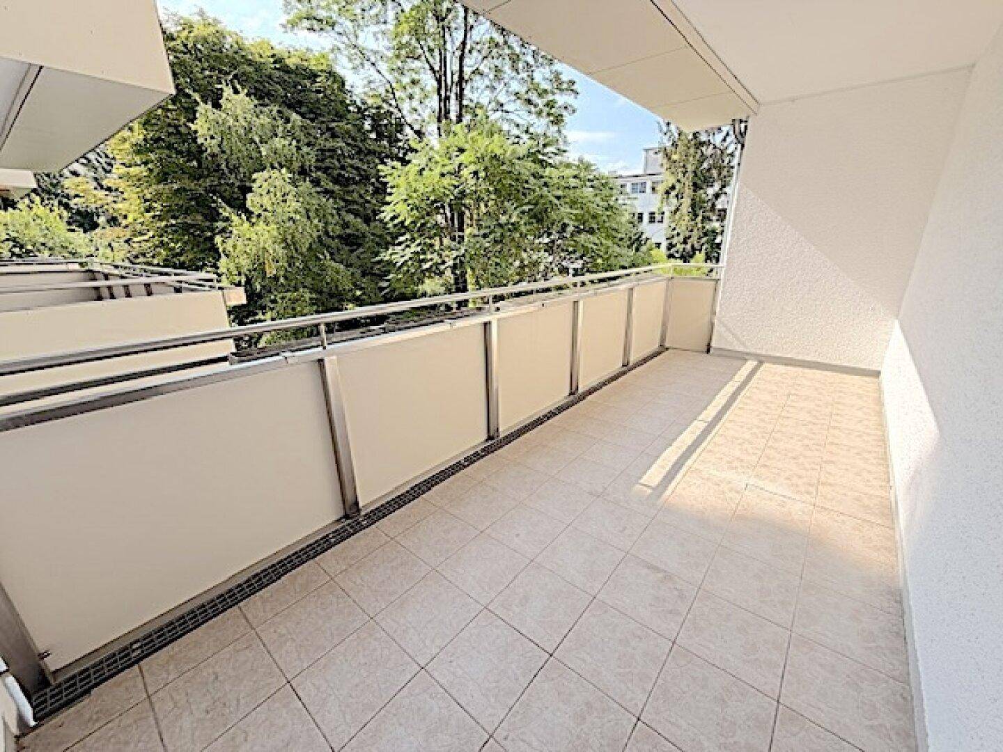 Geräumiger Balkon mit Fliesenboden und Blick auf grüne Bäume, ideal zum Entspannen.