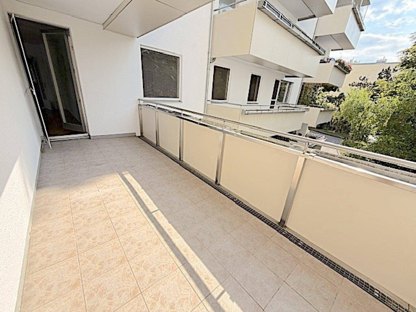 Geräumiger Balkon mit Fliesenboden und Blick auf die umliegenden Gebäude und Bäume.