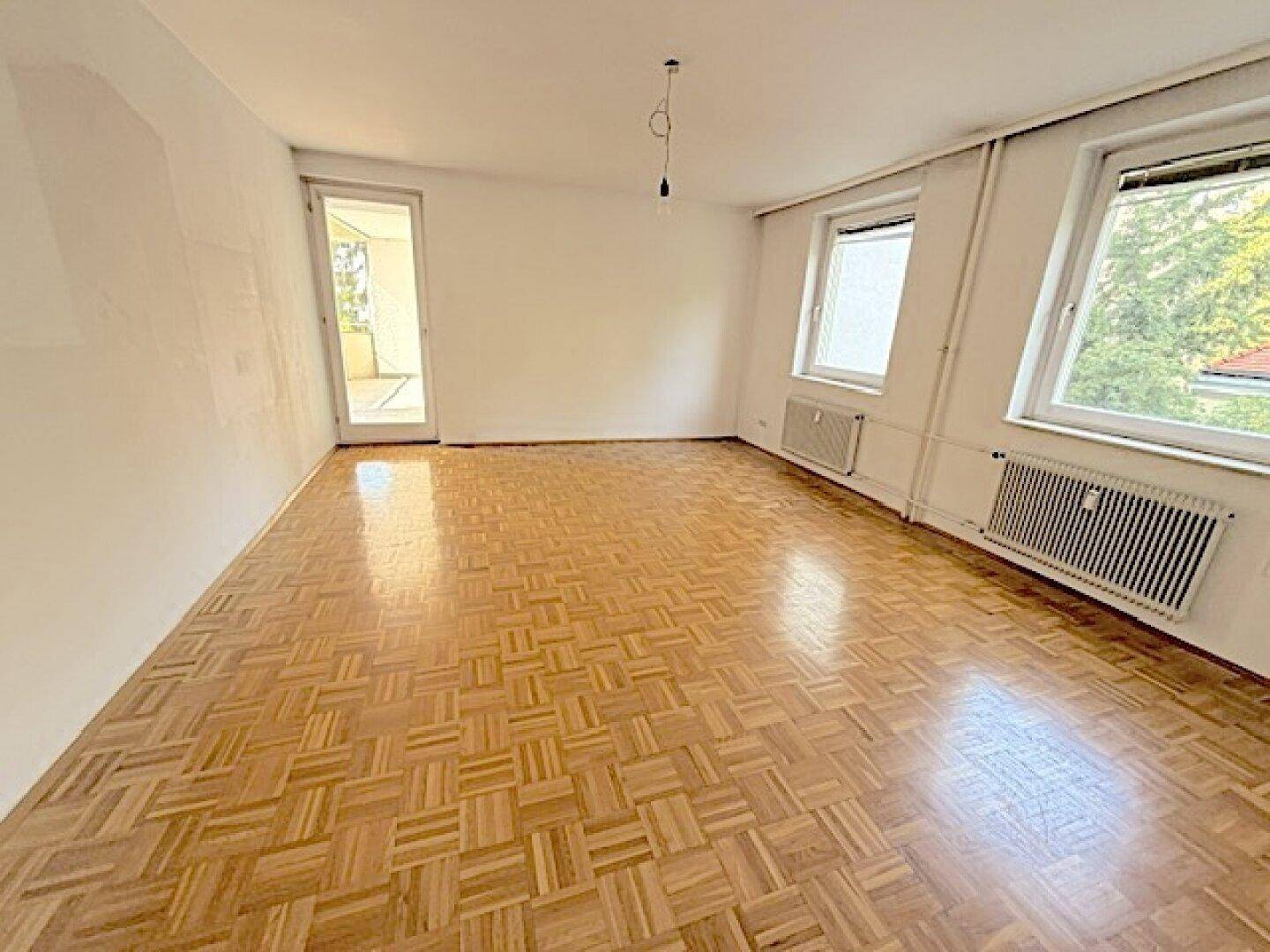 Großes, helles Wohnzimmer mit Fischgrätparkett und Zugang zu einem Balkon, ideal für geselliges Beisammensein.