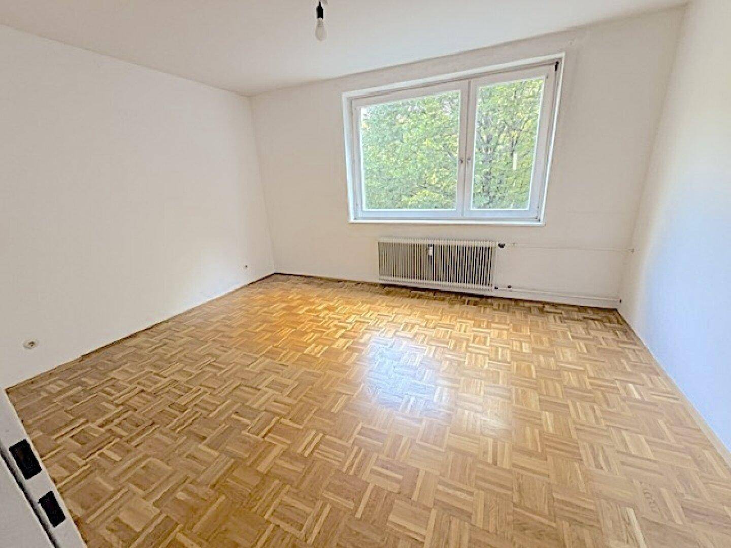 Geräumiges Schlafzimmer mit Fischgrätparkett und großem Fenster, das viel natürliches Licht hereinlässt.