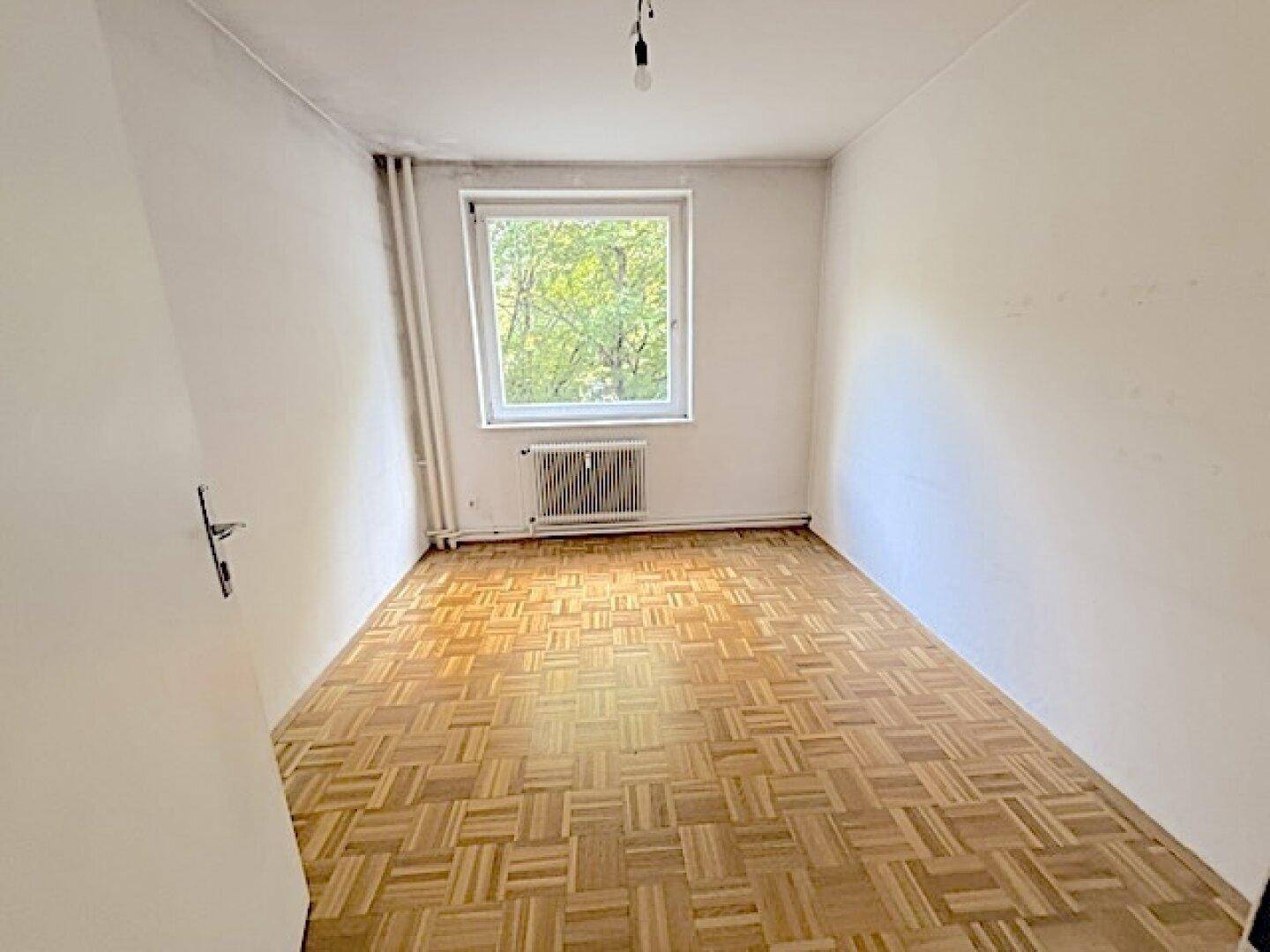 Helles Schlafzimmer mit Fischgrätparkett und großem Fenster, das eine angenehme Wohnatmosphäre schafft.