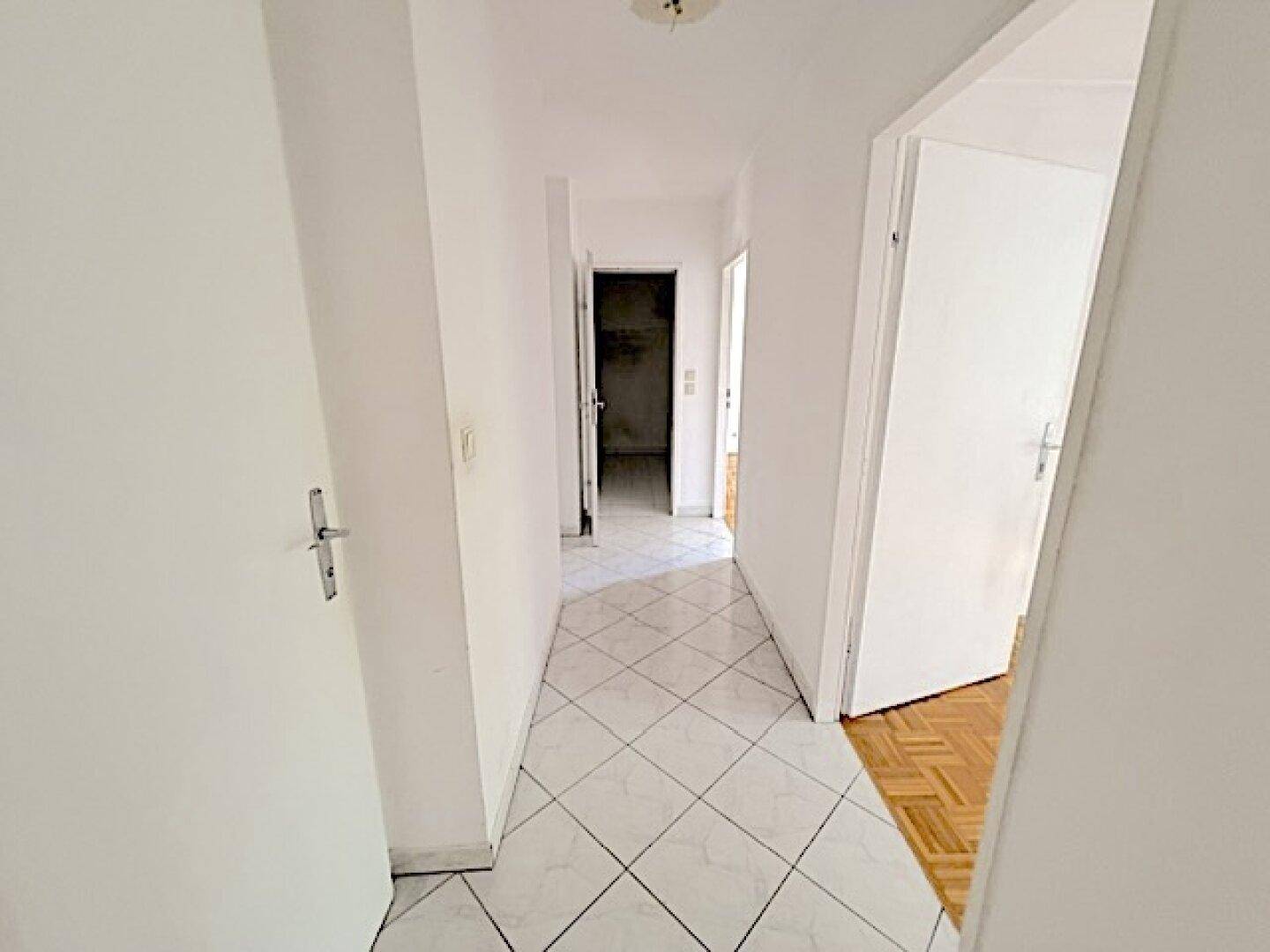 Langer, heller Flur mit weißen Fliesen, der verschiedene Räume der Wohnung miteinander verbindet.