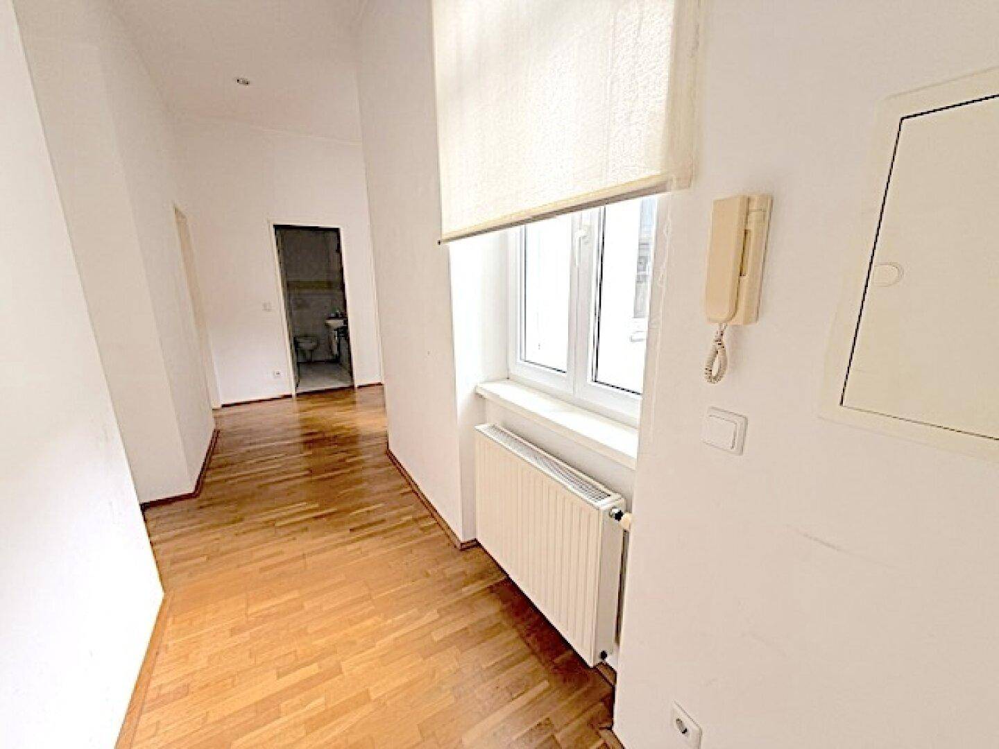 Heller Flur mit Parkettboden, Fenster und Gegensprechanlage an der Wand.