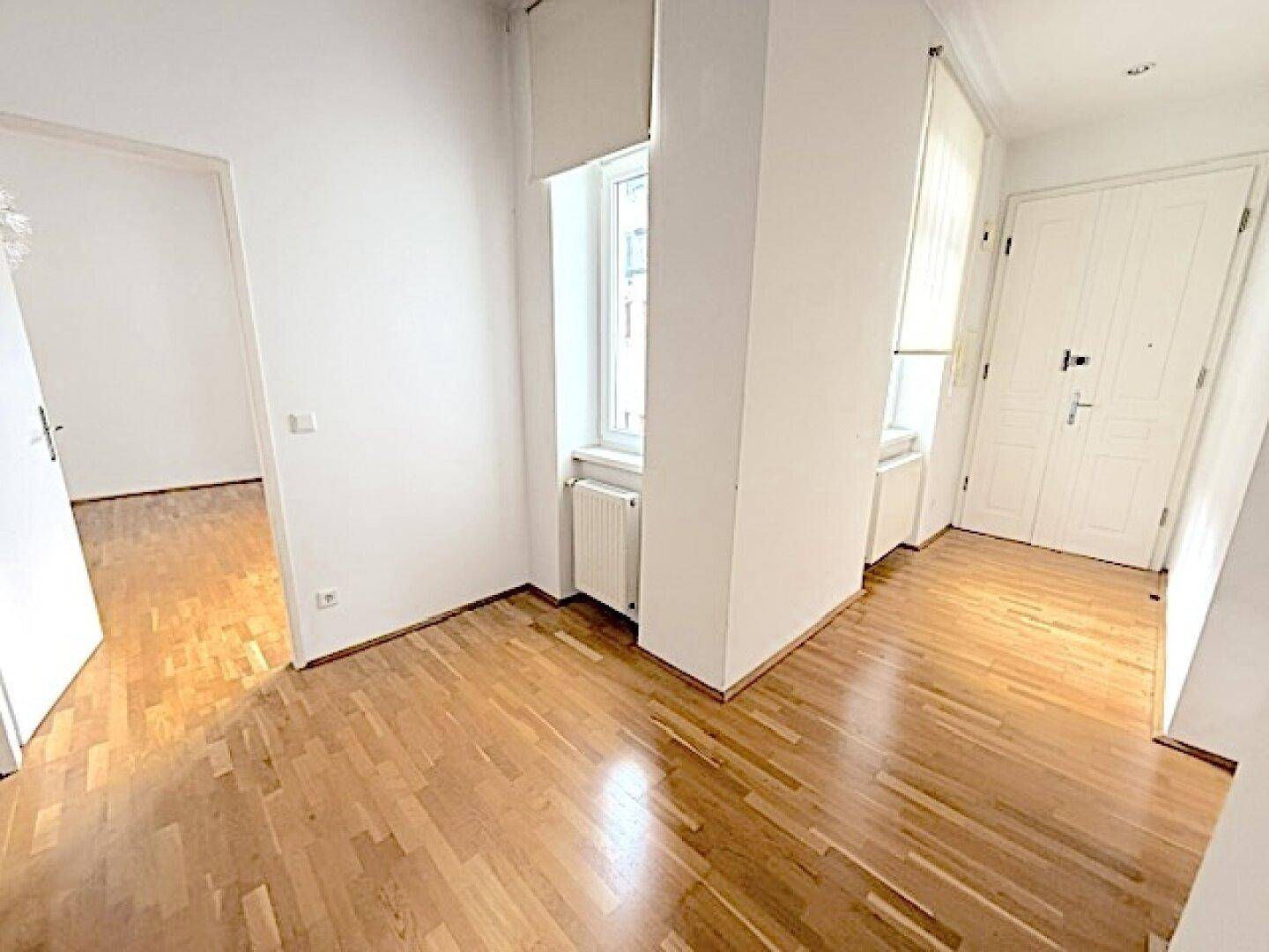 Eingangsbereich mit Parkettboden, Fenster und weißer Wohnungstür.