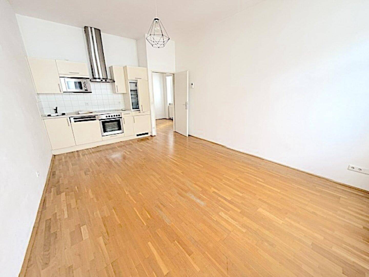 Offene Küche mit beigen Einbauschränken, Dunstabzugshaube und Parkettboden.