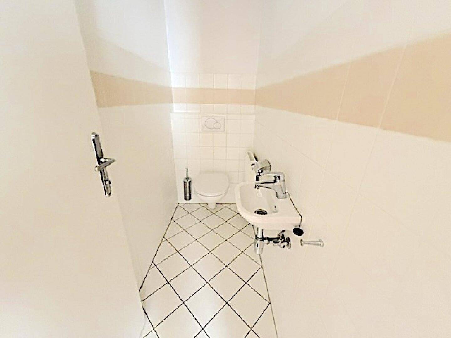 Kleines Gäste-WC mit diagonal gefliestem Boden, Toilette und Handwaschbecken.
