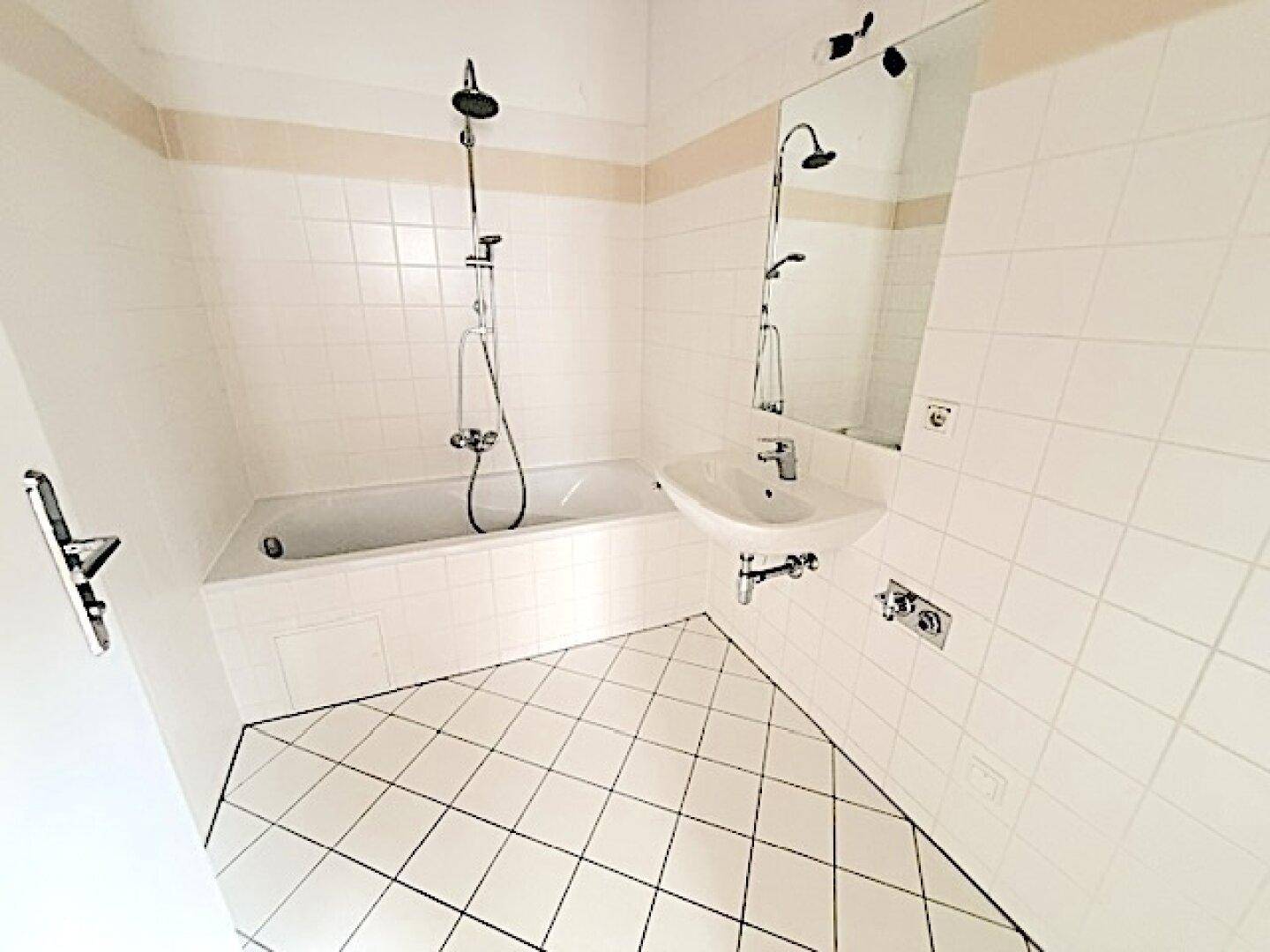 Badezimmer mit Badewanne, Dusche, Waschbecken und weiß-beigen Fliesen.