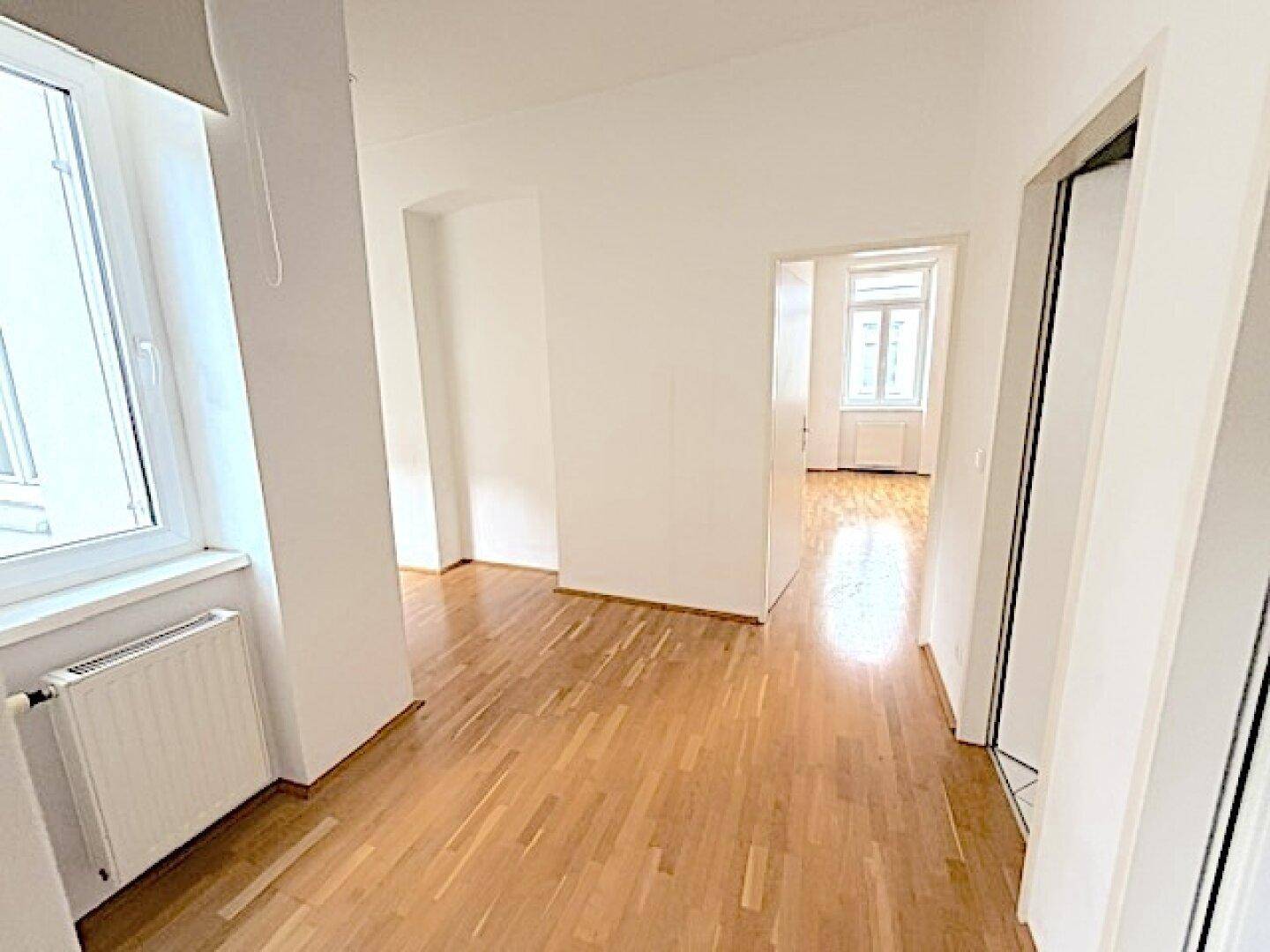 Langer Flur mit Parkettboden, Fenster und mehreren Türen zu angrenzenden Räumen.