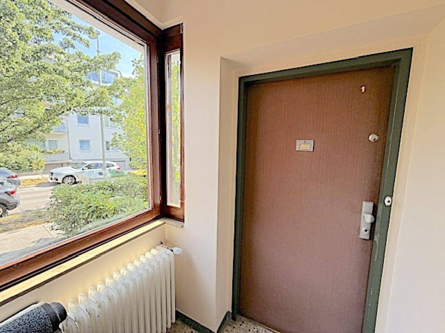 Eingangsbereich mit Fenster und Heizkörper, bietet einen Blick auf die Straße und parkende Autos.