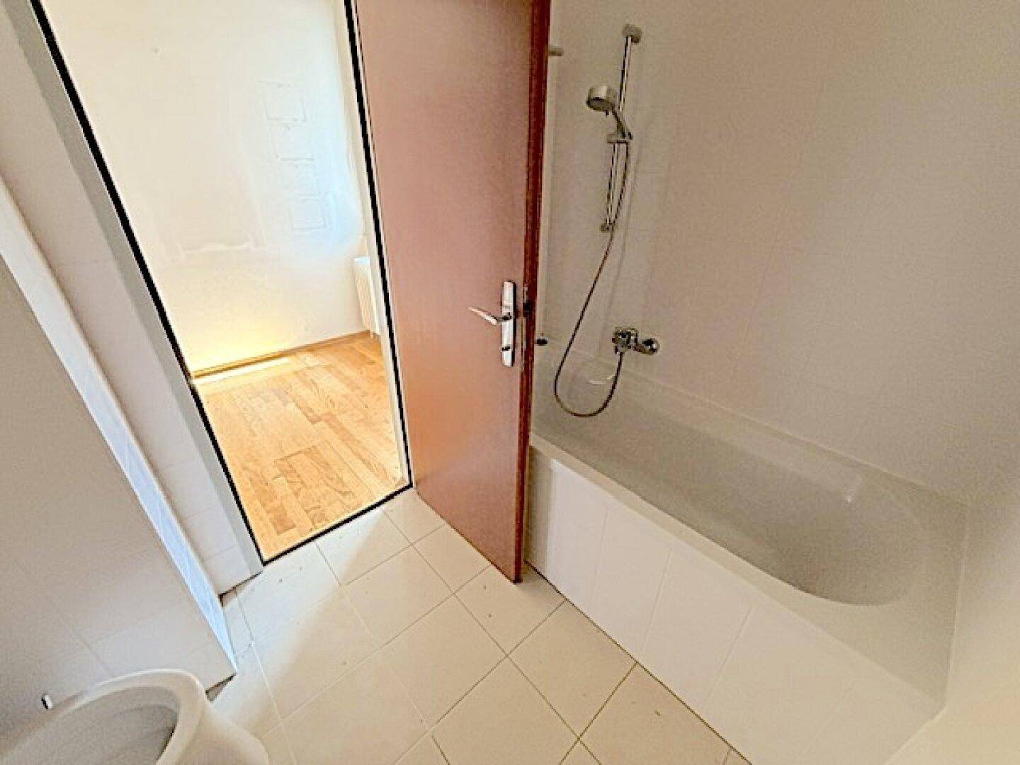 Badezimmer mit Badewanne und Duscharmatur, angrenzend an einen weiteren Raum.
