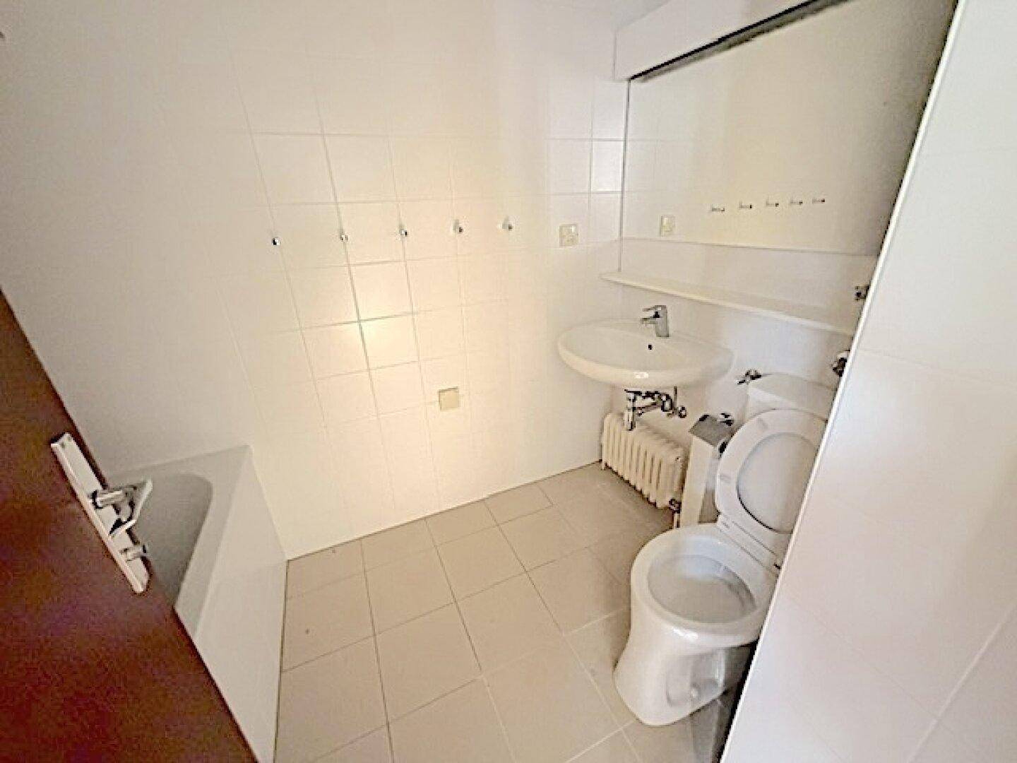 Badezimmer mit WC, Waschbecken und weißen Fliesen, bereit für eine Modernisierung.