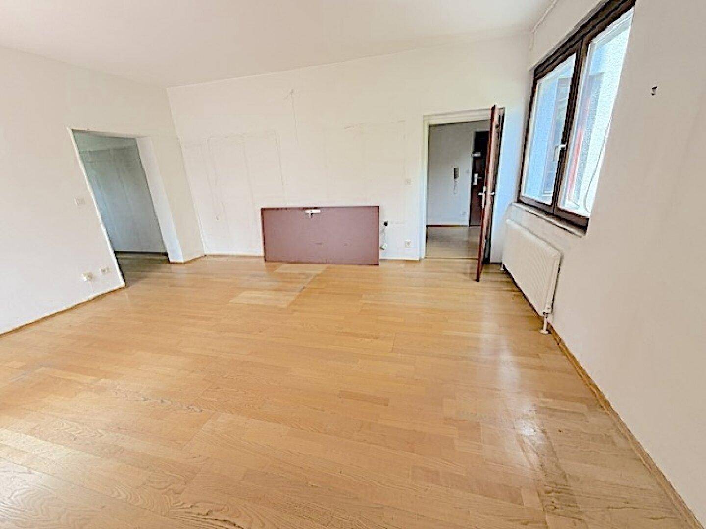 Geräumiges Wohnzimmer mit Parkettboden und Zugang zu weiteren Räumen, hell und einladend.