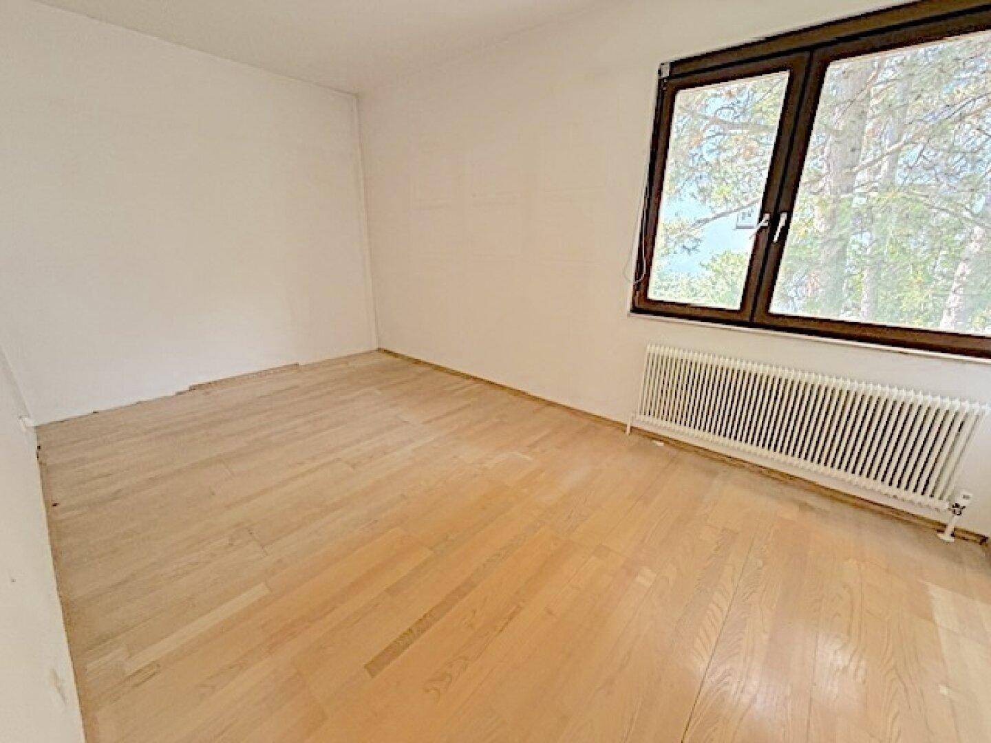 Ruhiges Zimmer mit Parkettboden und großem Fenster, ideal als Schlaf- oder Arbeitszimmer.