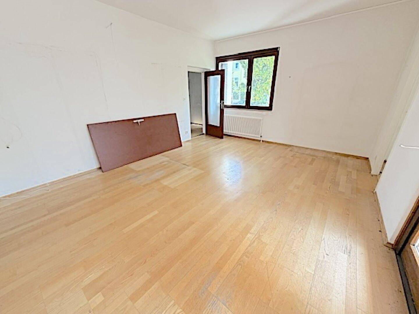 Helles Zimmer mit Parkettboden und großem Fenster, bietet viel Tageslicht und Raum.