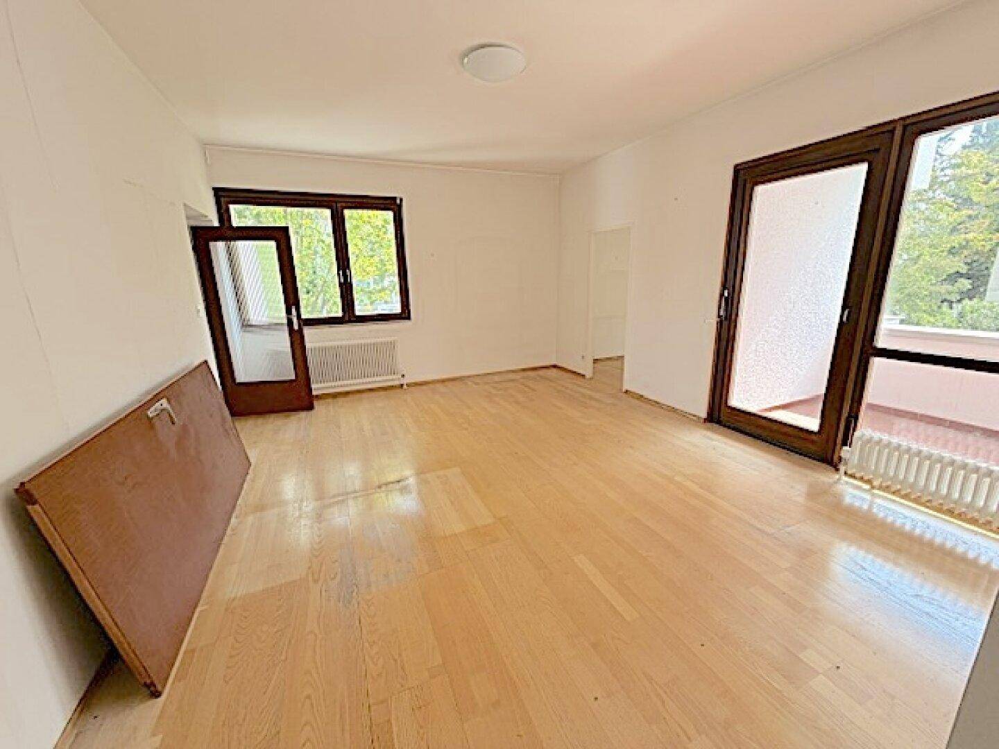 Großes Wohnzimmer mit Parkettboden und Zugang zum Balkon, bietet viel Licht und Platz.