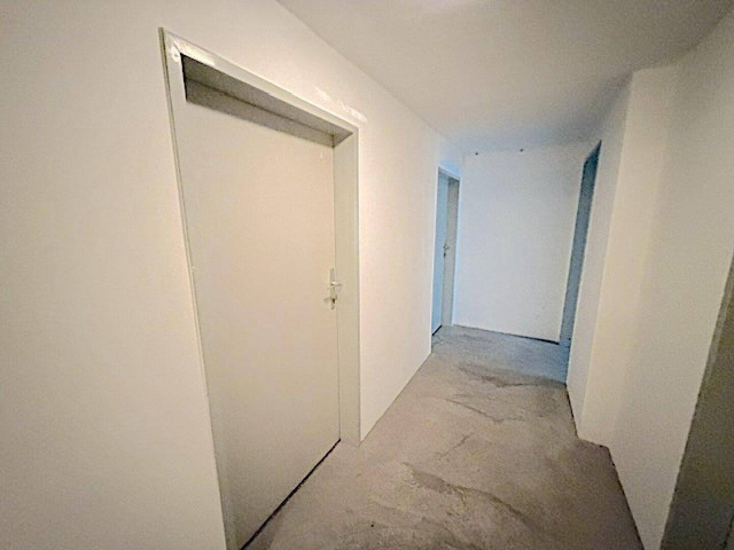 Heller Flur im Untergeschoss mit Betonboden und Zugang zu weiteren Räumen.