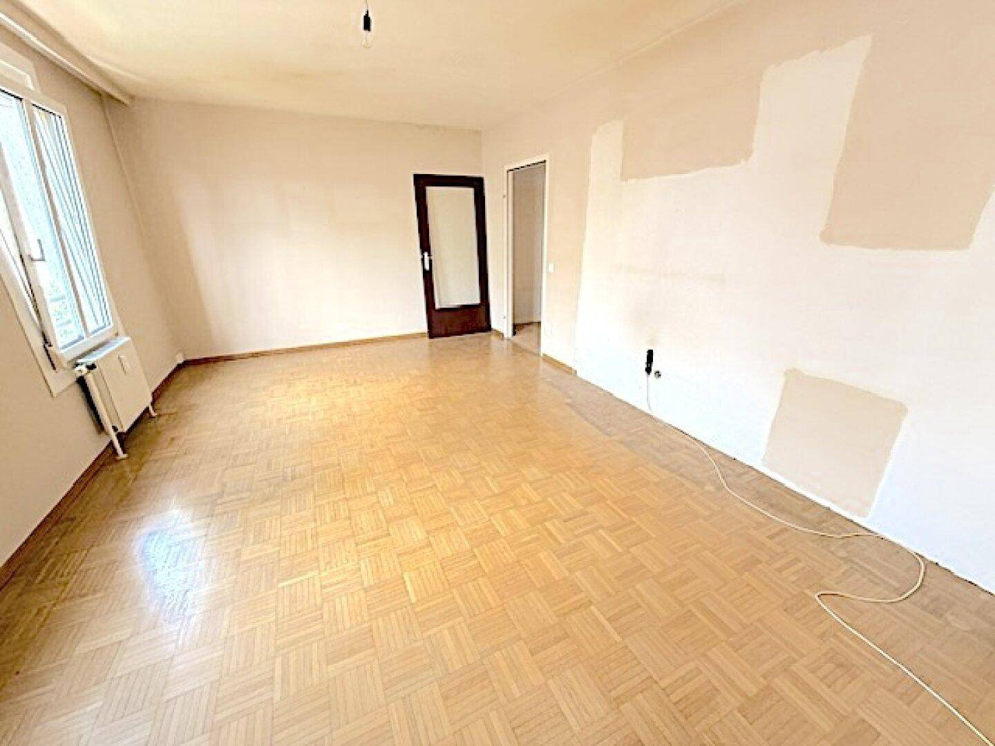 Geräumiges, leeres Zimmer mit Parkettboden und einem Fenster, ideal für Wohnzwecke.