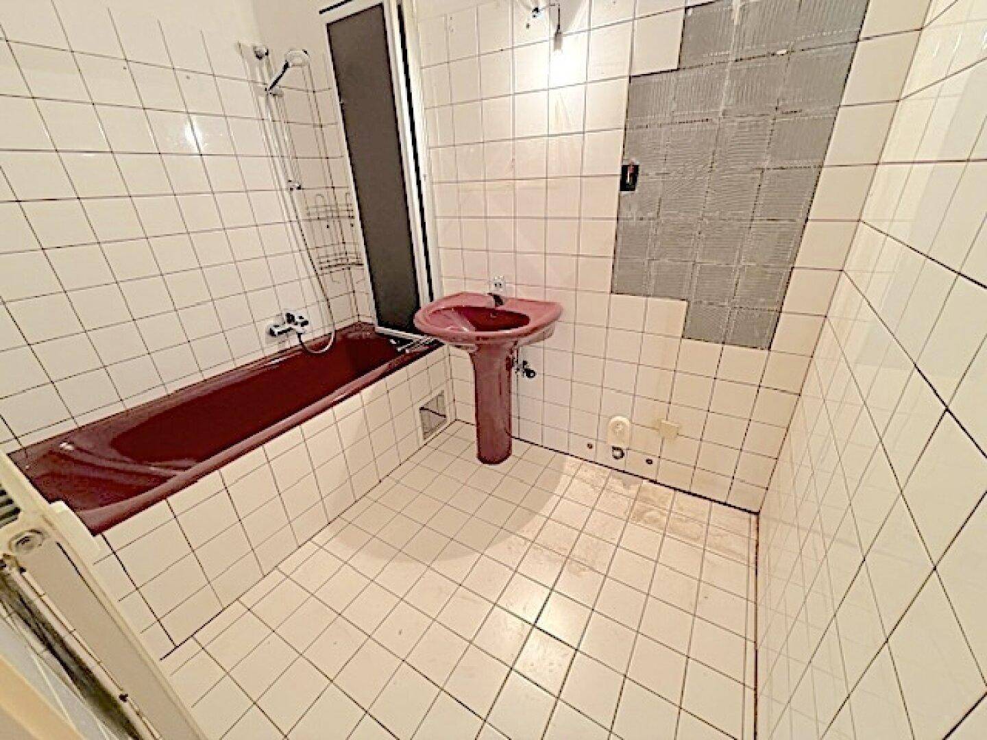 Badezimmer mit roter Badewanne und Waschbecken, umgeben von weißen Wandfliesen.