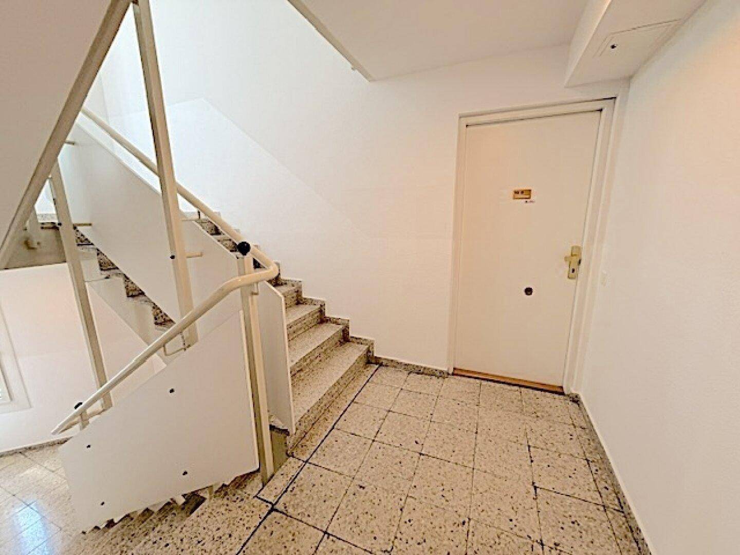 Treppenhaus mit Terrazzoboden und weißen Geländern, führt zu den oberen Etagen.