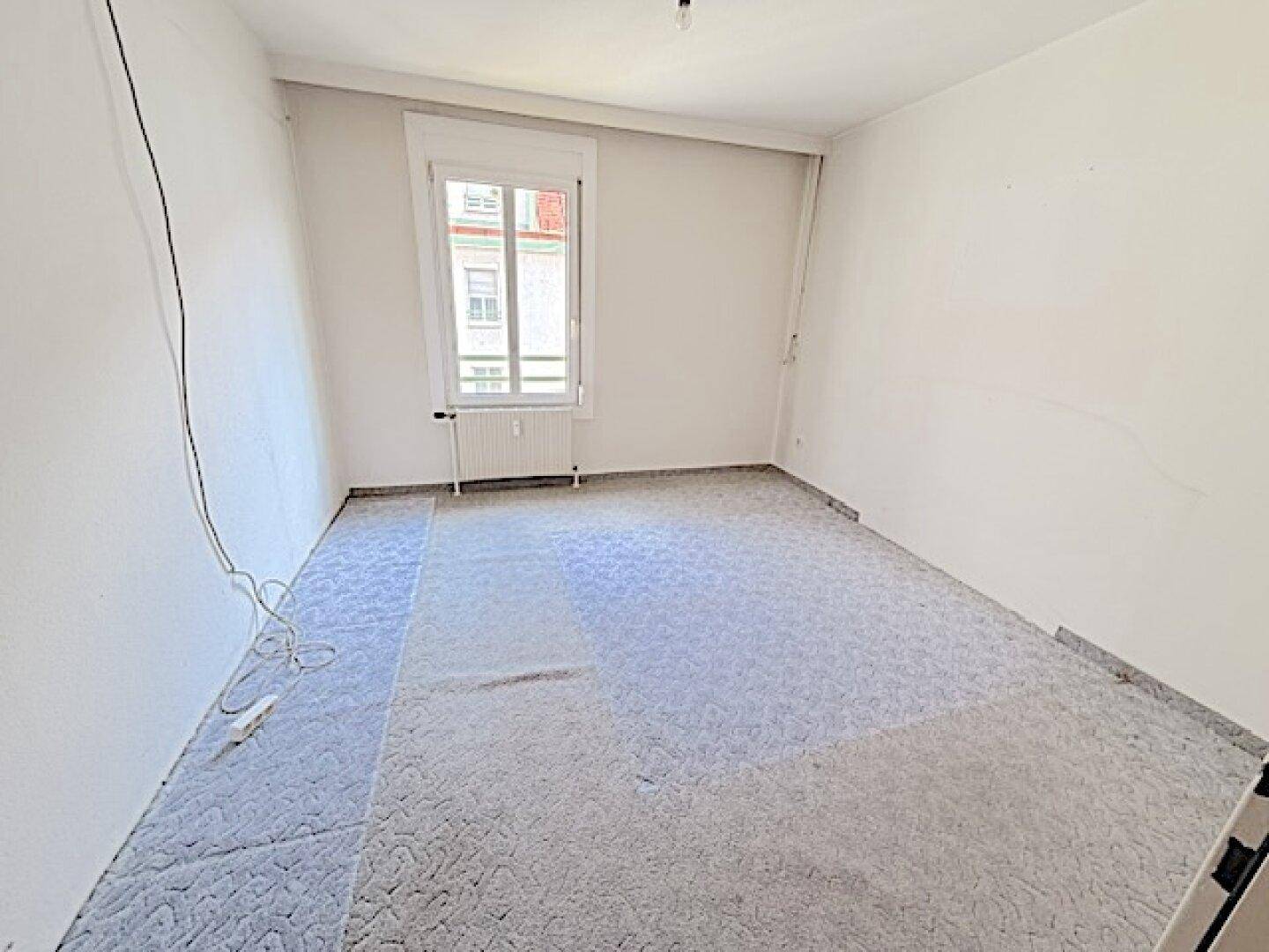 Leeres Zimmer mit Fenster und gemustertem Bodenbelag, bereit zur individuellen Einrichtung.