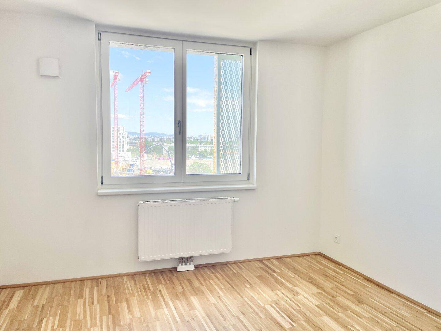 Helles Zimmer mit Parkettboden und Fenster, das einen Blick auf die Stadt und Baustellen bietet.