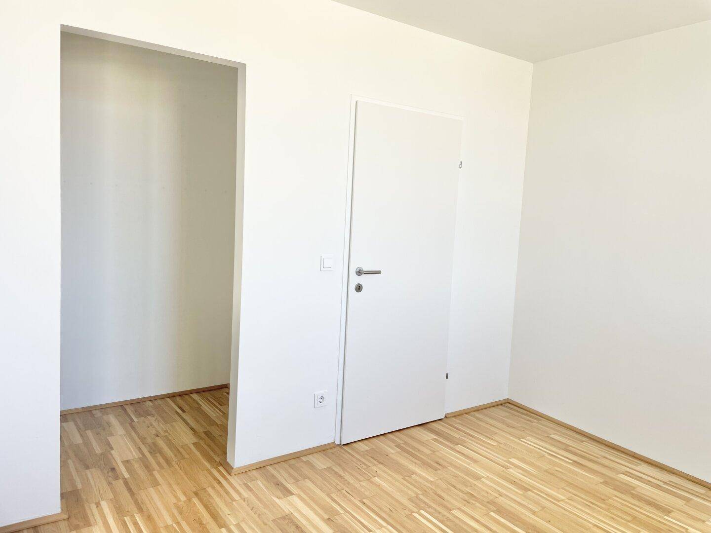 Leerer Raum mit Parkettboden und weißer Tür, der vielseitig genutzt werden kann.